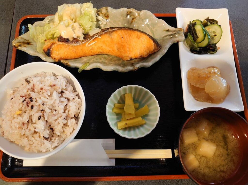 Example of teishoku meal, arranged in ichiju sansai pattern. In the bottom left, a bowl of rice; moving to the right, pickles and miso soup. The side dishes are grilled salmon, vinegared and simmered vegetables.